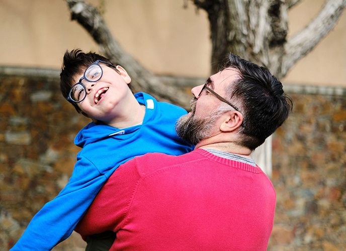 Loving father holding and playing with his disabled son while enjoying time together outdoors. Disabled people and parenthood concept.